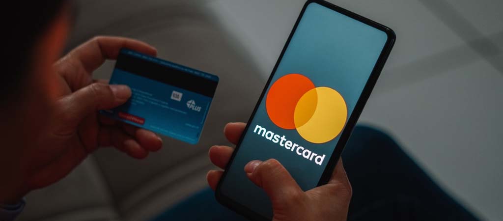 Mastercard logó, mobiltelefon képernyő, bankkártya a kézben, online fizetés, digitális tranzakció, pénzügyi szolgáltatás